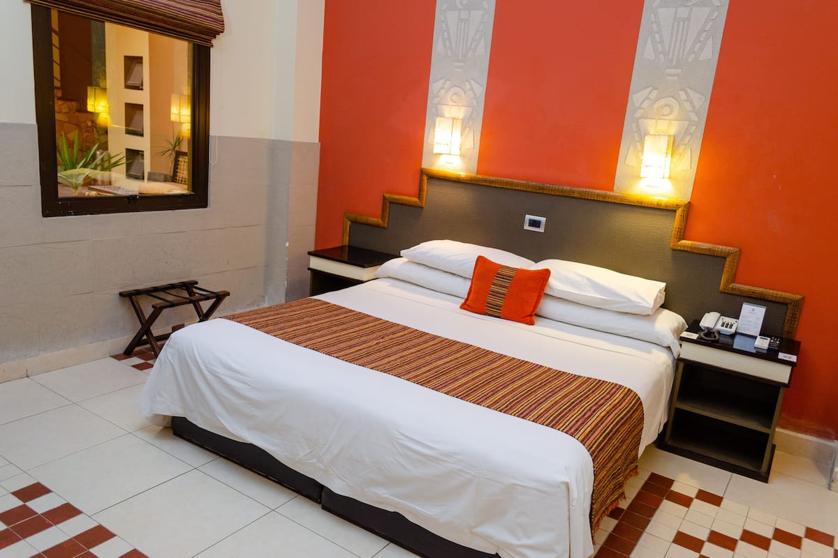 Una habitación de hotel con cama, mesitas de noche, un espejo y una pequeña mesa.