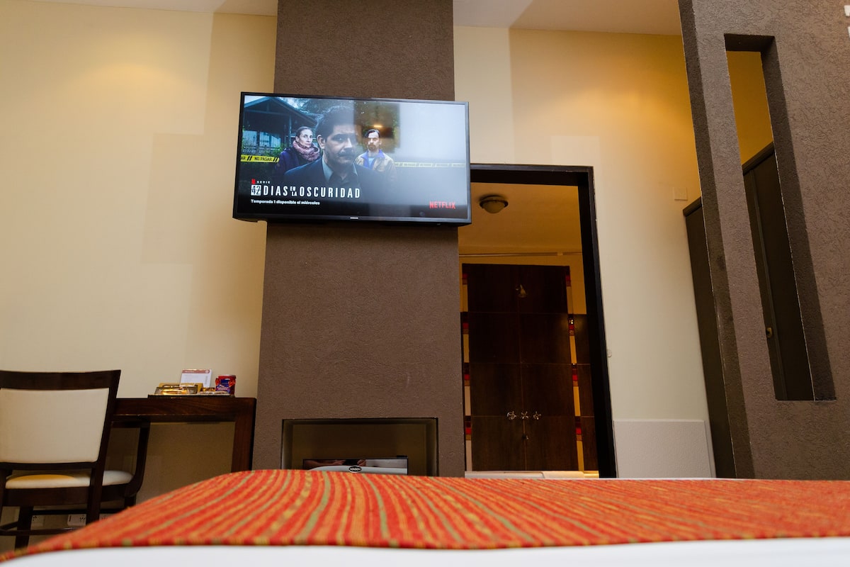 Habitación de hotel con cama, escritorio, silla, televisor montado en la pared y puerta que da a otra habitación.