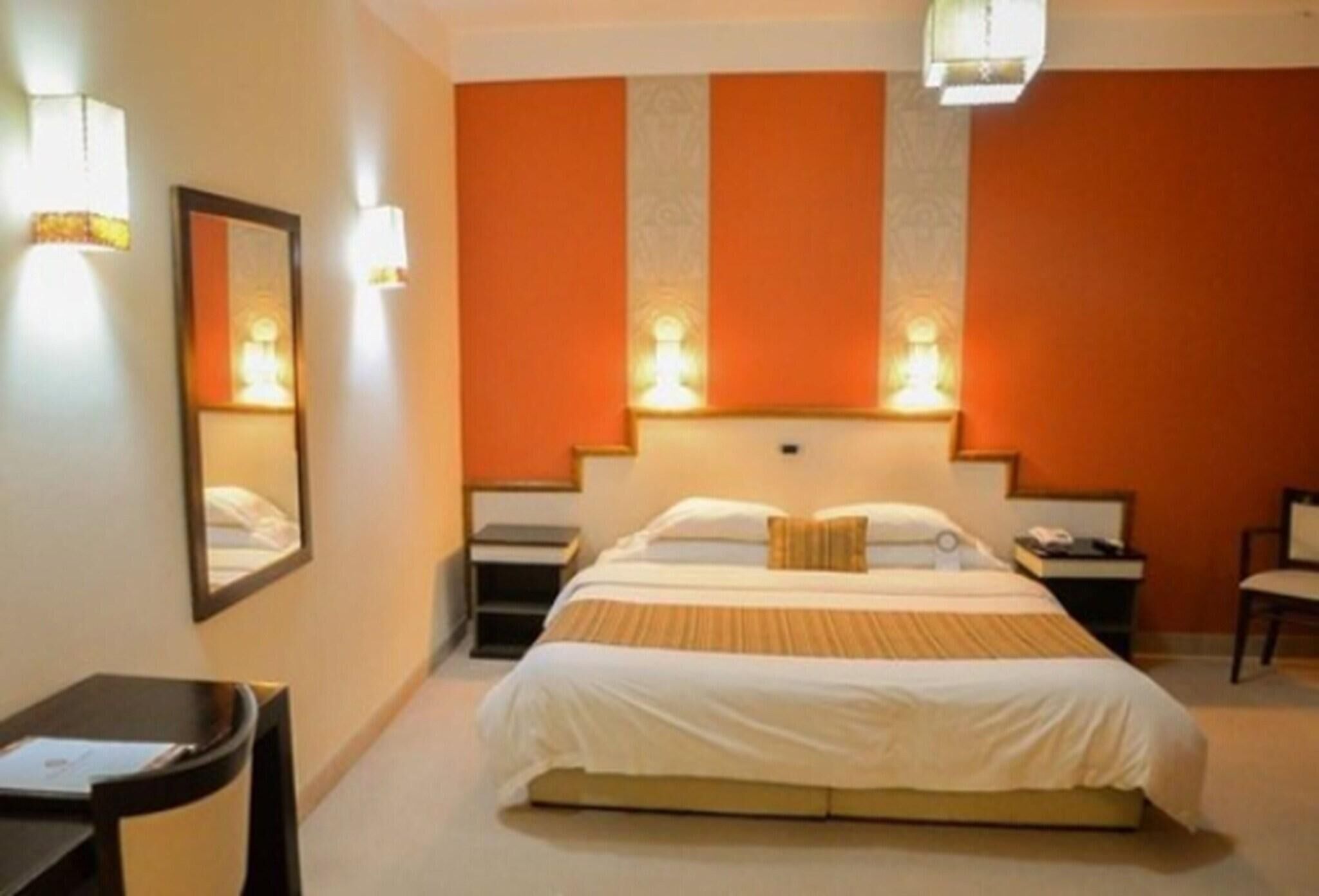 A hotel room with a bed, bedside tables, a chair, a desk, and a mirror.