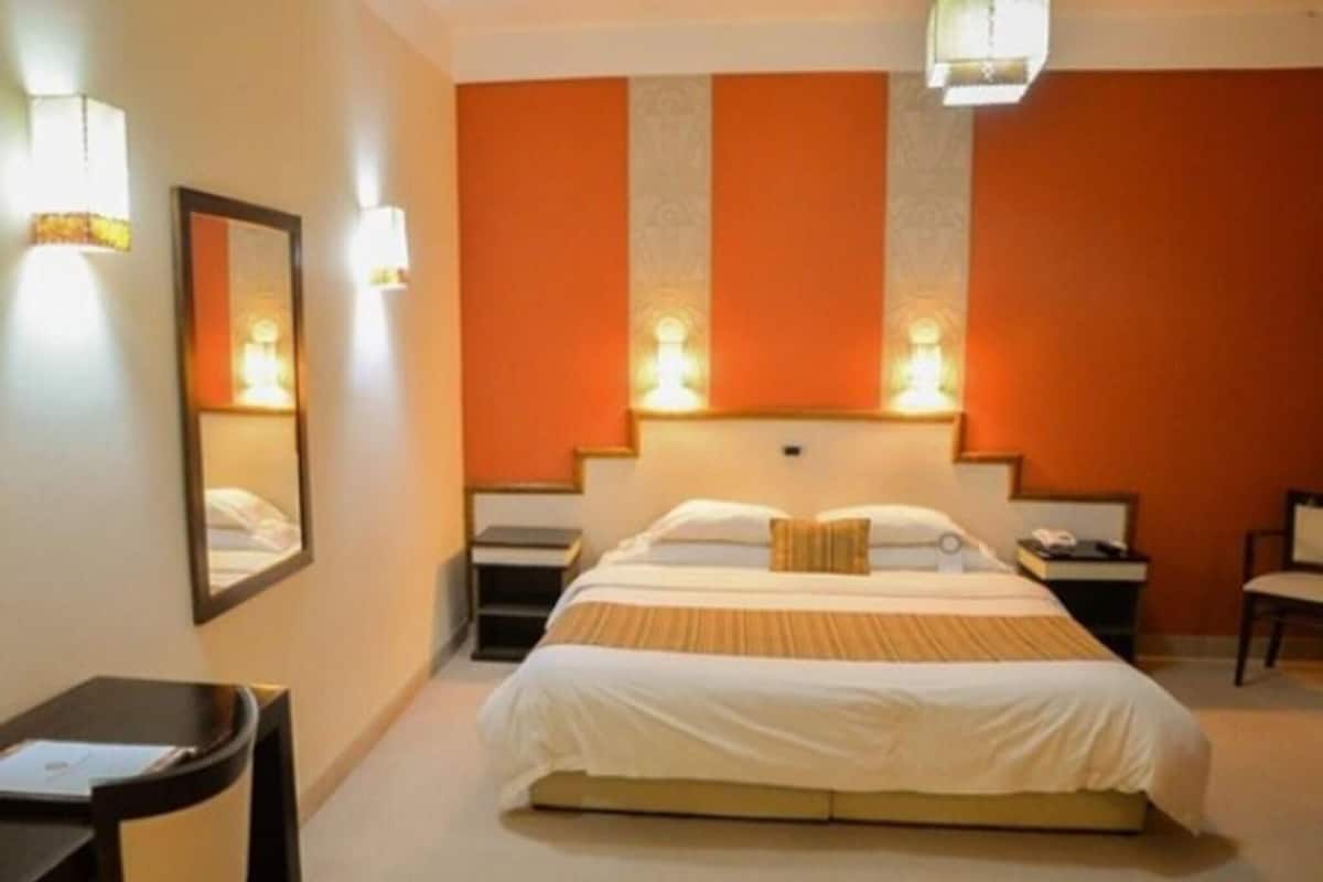 Una habitación de hotel con cama, mesitas de noche, una silla, un escritorio y un espejo.