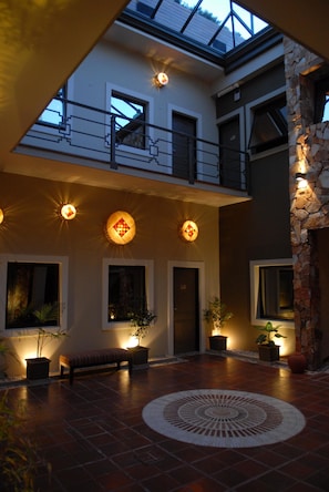 Um pátio espaçoso com um desenho circular central, um banco, plantas em vasos e uma parede de pedra.