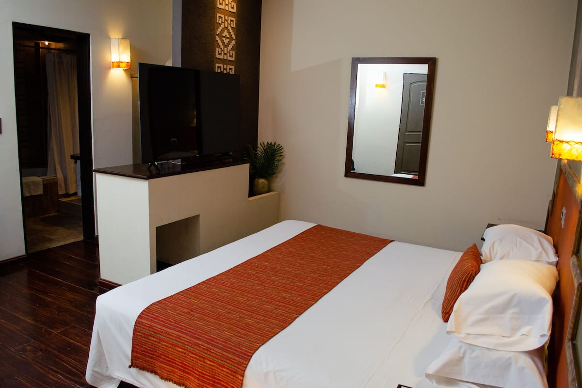 Habitación de hotel con cama, televisor, espejo y lámpara de pared.