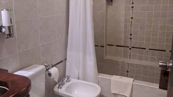 Un baño con inodoro, bidé, ducha y un televisor montado.