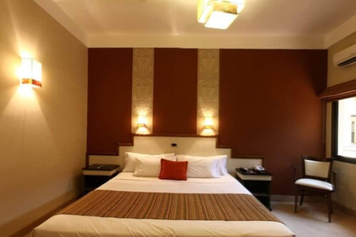 Una habitación de hotel con una cama grande, dos mesitas de noche, una silla y un ventanal.