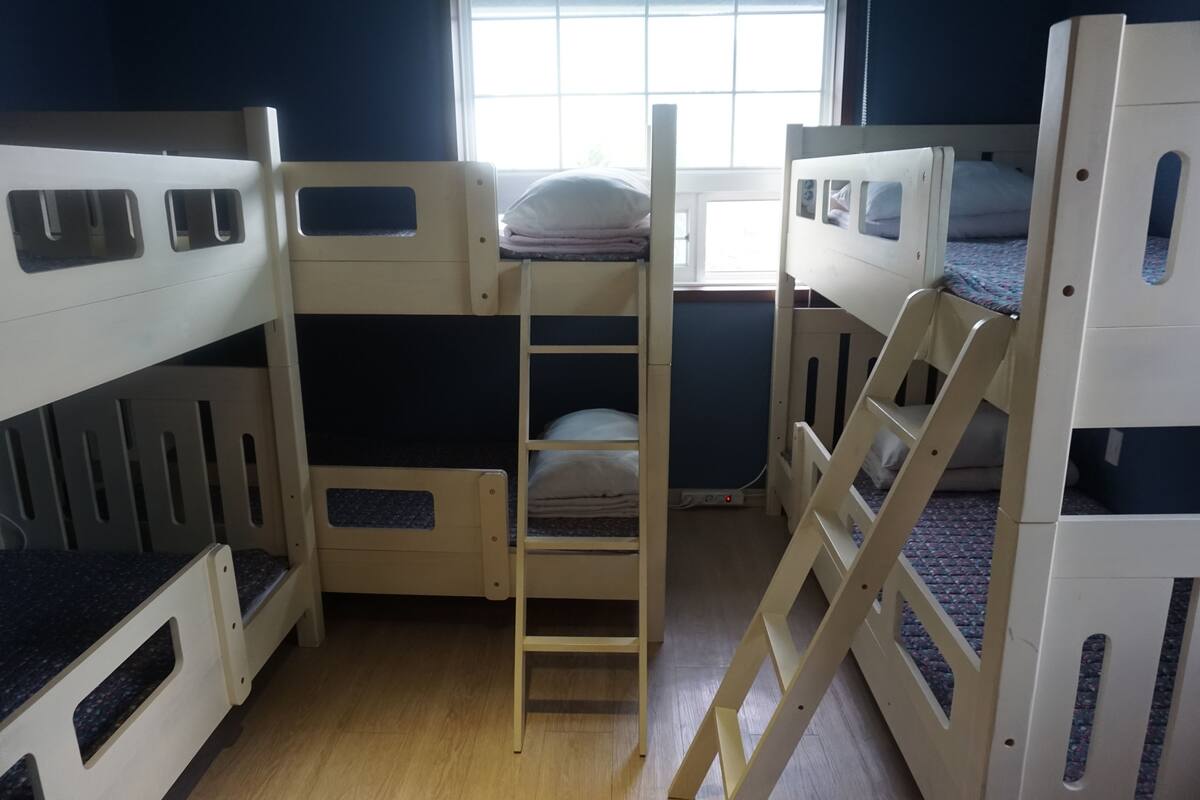A bunk bed room with a ladder connecting the beds, a window with blinds, and a wooden floor.