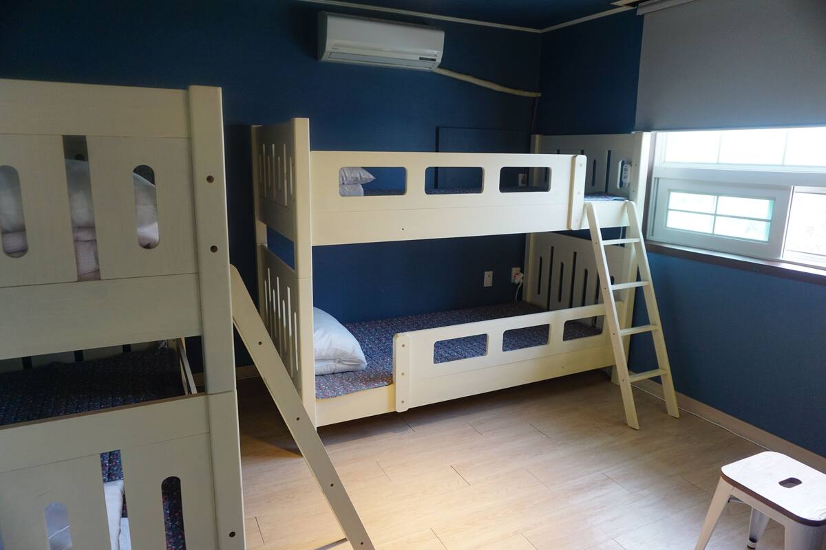 A bunk bed room with a window, a white desk, and a ladder.