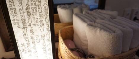 Une pièce avec un plancher en bois, un panier en osier rempli de serviettes pliées et un panneau avec du texte.