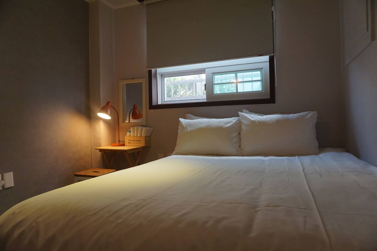 A neatly made bed with white linens in a room with a small table and two lamps.