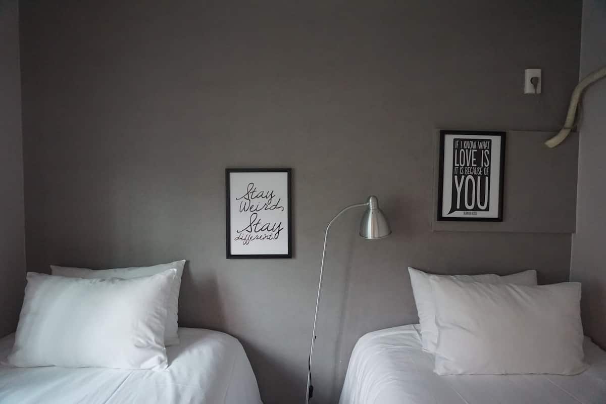 A hotel room with two single beds, a bedside lamp, and two motivational posters on the wall.