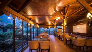 A restaurant with wooden beams, wicker chairs, and a view of a garden through large windows. - WULAI SungLyu spring resort (New Taipei City)