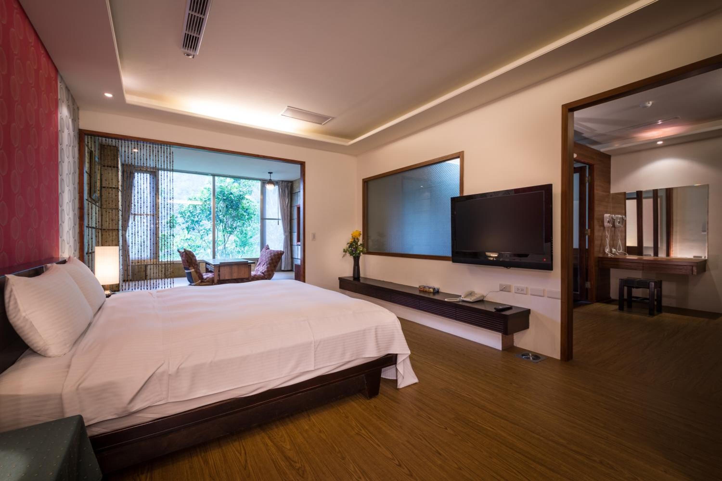 Una camera d'albergo moderna con un letto grande, una TV a parete, una scrivania con una sedia e vista sul verde.