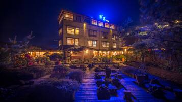 A multi-story hotel with a well-lit entrance and a garden area with potted plants and a wooden deck.