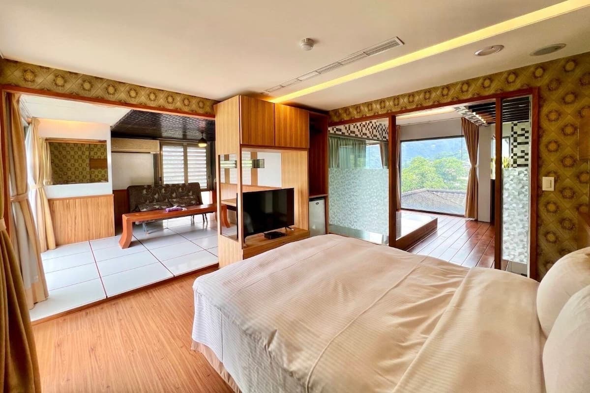 A bedroom with a large bed, a TV, and a seating area with a view of the outdoors.