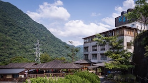 A traditional Japanese building with a wooden structure and a modern extension, surrounded by lush greenery and mountains. - WULAI SungLyu spring resort (New Taipei City)