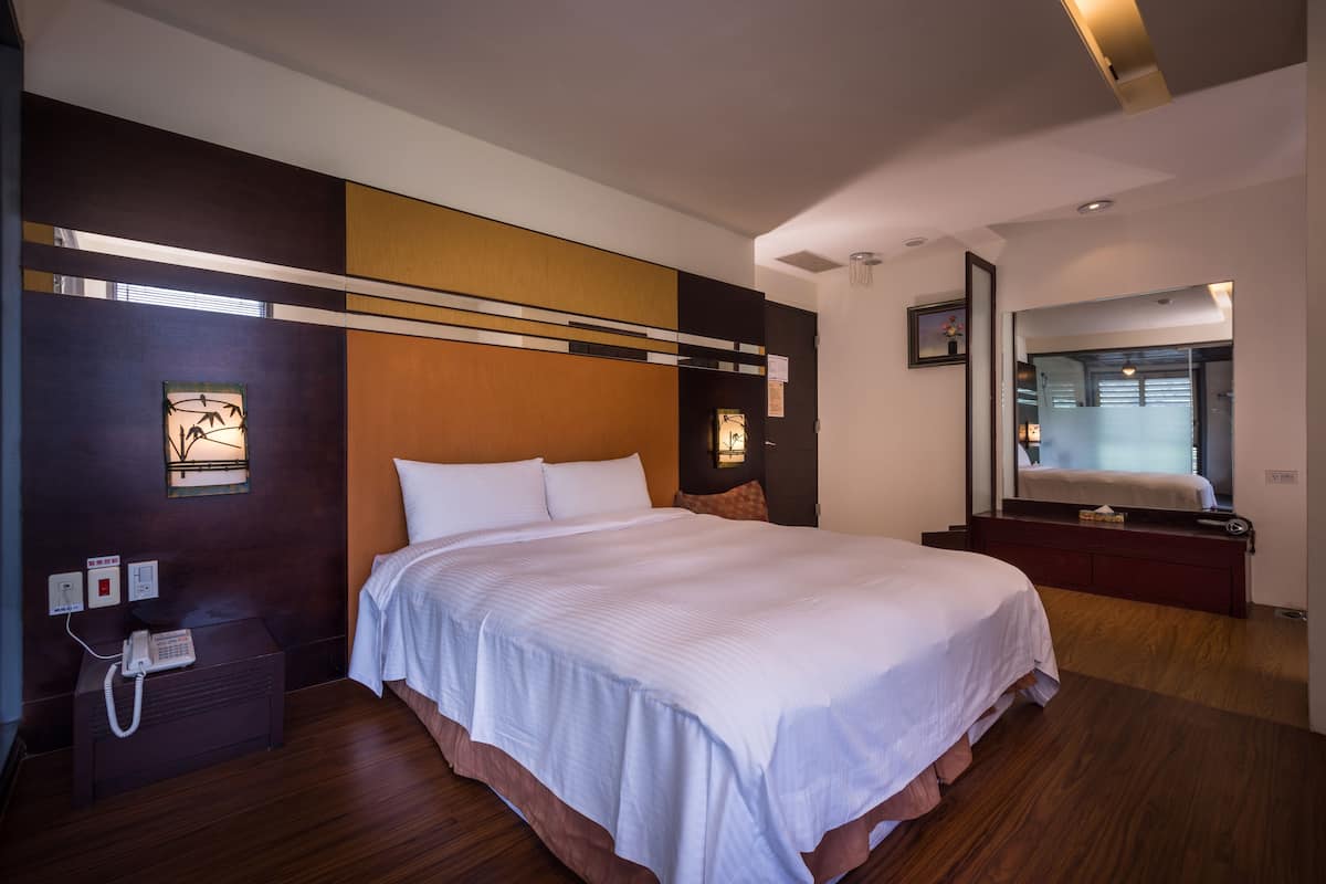 A modern hotel room with a large bed, a bedside table with a phone, a mirror, and a view of the bathroom.