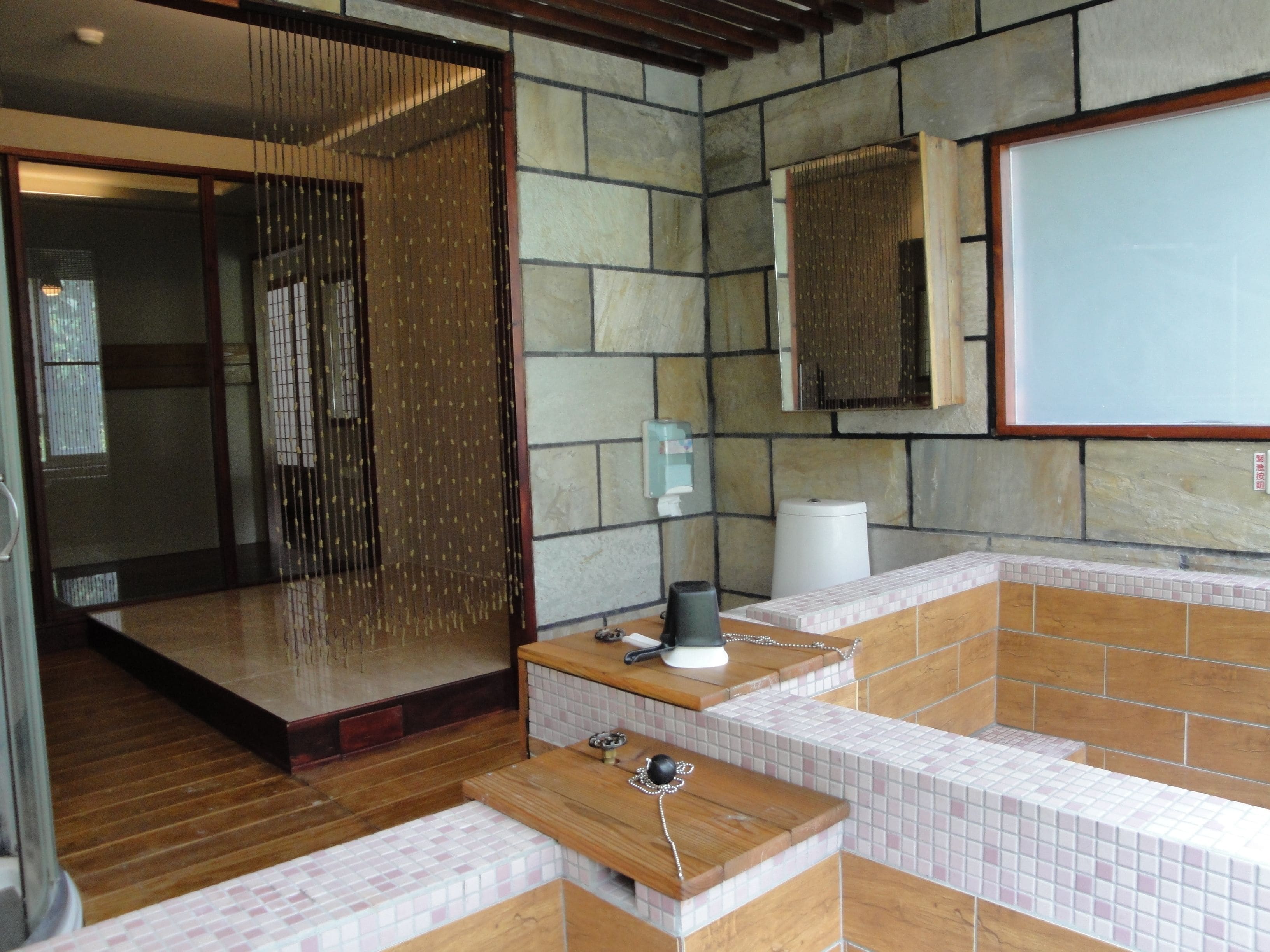 Un bagno moderno con parete in pietra, una panca in legno, cabina doccia in vetro e un water.