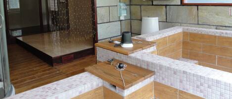 Un bagno moderno con parete in pietra, una panca in legno, cabina doccia in vetro e un water.