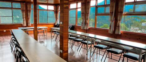 A large room with long tables and chairs, wooden floors, and large windows with curtains.
