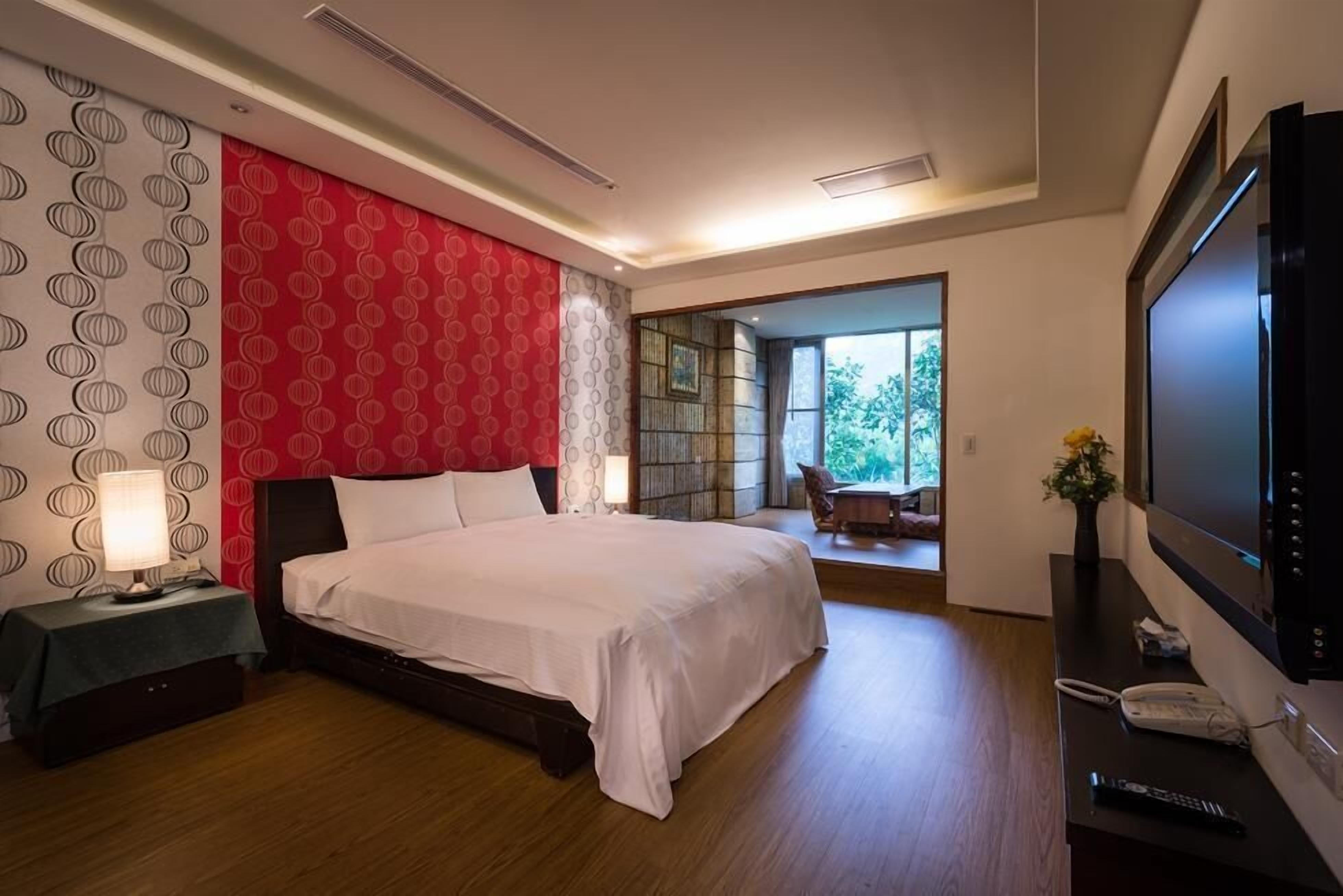 A modern hotel room with a large bed, a TV, a desk with a phone, and a view of the outdoors.