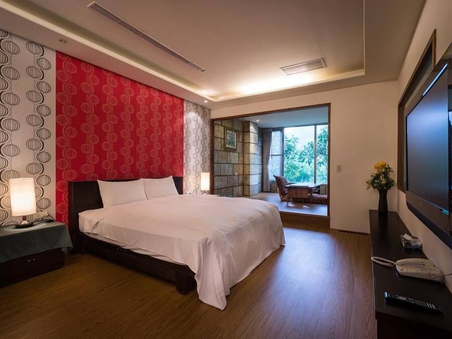 A modern hotel room with a large bed, a TV, a desk with a phone, and a view of the outdoors.