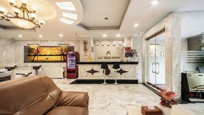 Un hall d’hôtel moderne avec un sol en marbre, un canapé en cuir, un comptoir d’accueil et un grand tableau accroché au mur.