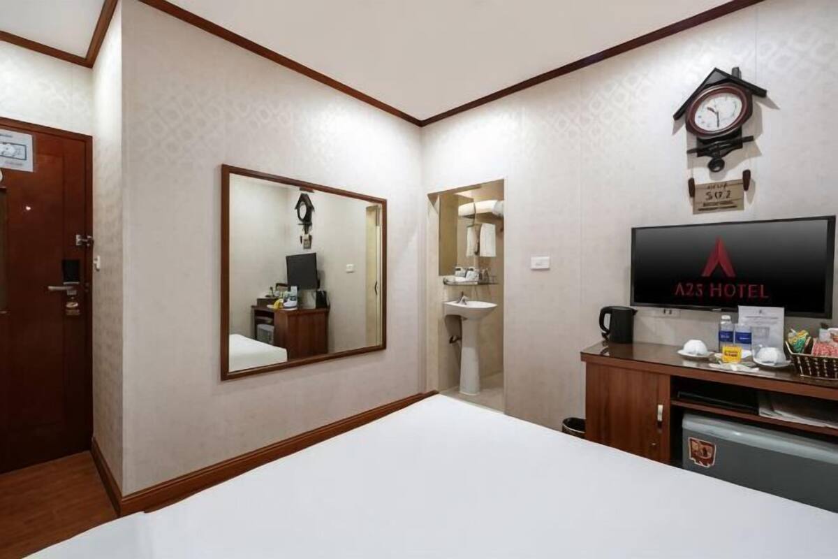 A hotel room with a bed, a television, a clock, a mirror, and a small kitchenette.