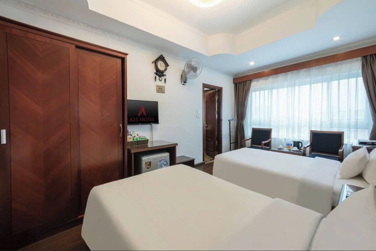 A hotel room with two beds, a TV, a clock, a fan, and a desk with a computer.