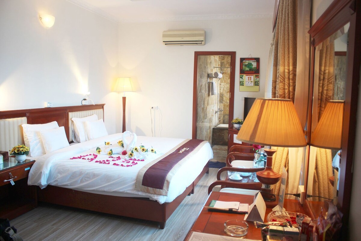 Une chambre d’hôtel dotée d’un grand lit, de tables de chevet, d’un bureau, d’une chaise, d’une lampe, d’un climatiseur et d’un espace douche.