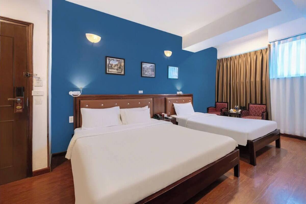 A hotel room with two beds, a wooden headboard, a desk with a chair, and a window with curtains.