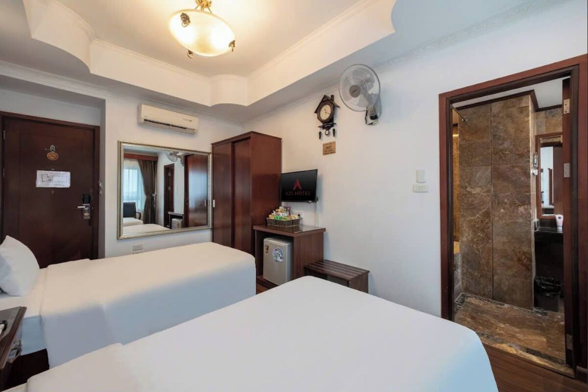 A hotel room with two beds, a small refrigerator, a clock, and a mirror on the wall.
