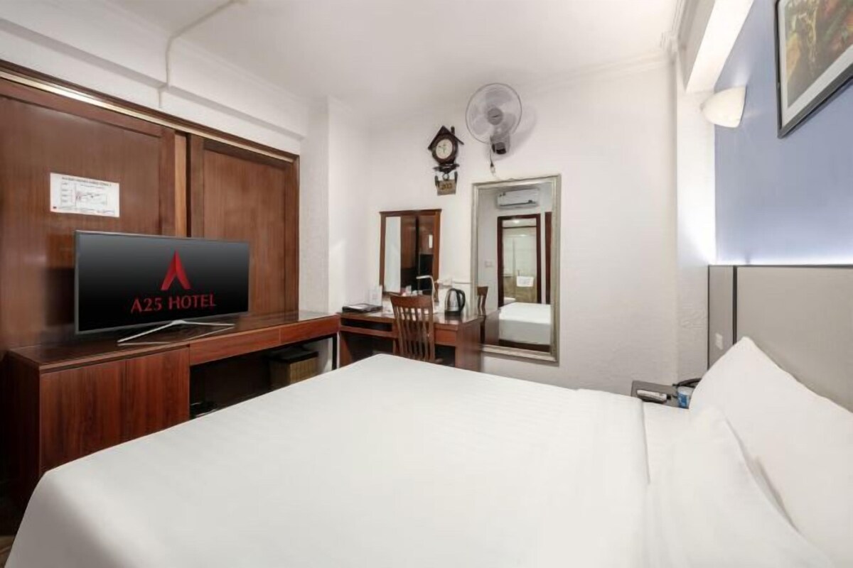 Een hotelkamer met een bed, een bureau met stoel, een televisie, een klok en een spiegel.