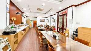 A restaurant with wooden flooring, glass tables, and chairs. There is a counter with a statue and a sign above it.