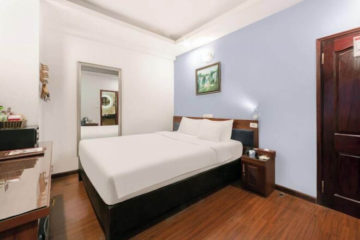 Una habitación de hotel con cama, mesita de noche y un reloj en la pared.