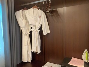 Une chambre d’hôtel avec une armoire en bois, un peignoir accroché à la porte et une table sur laquelle se trouvent un bloc-notes et un stylo.