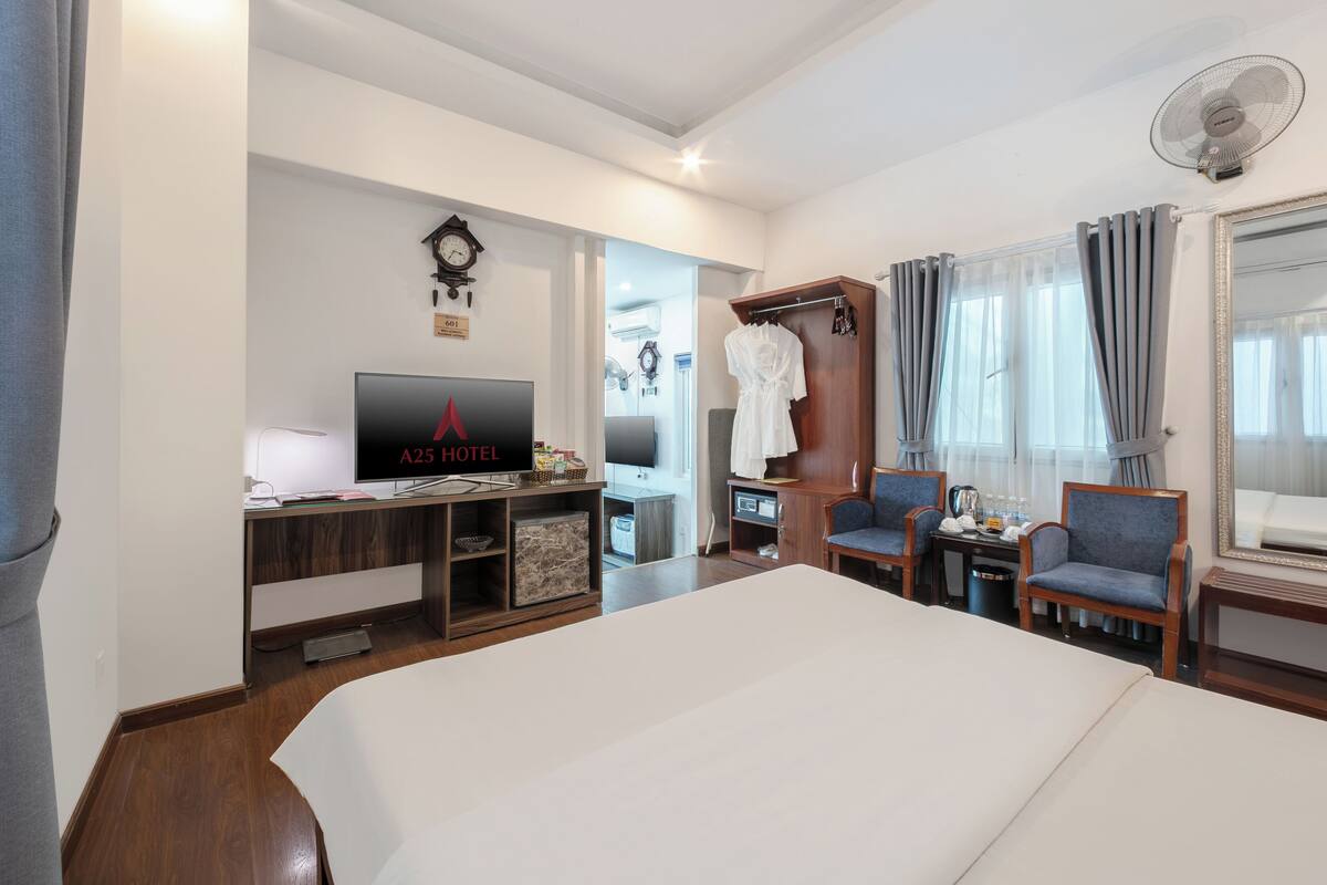 A hotel room with a bed, a TV, a desk with a computer, a wardrobe, and a seating area with chairs.
