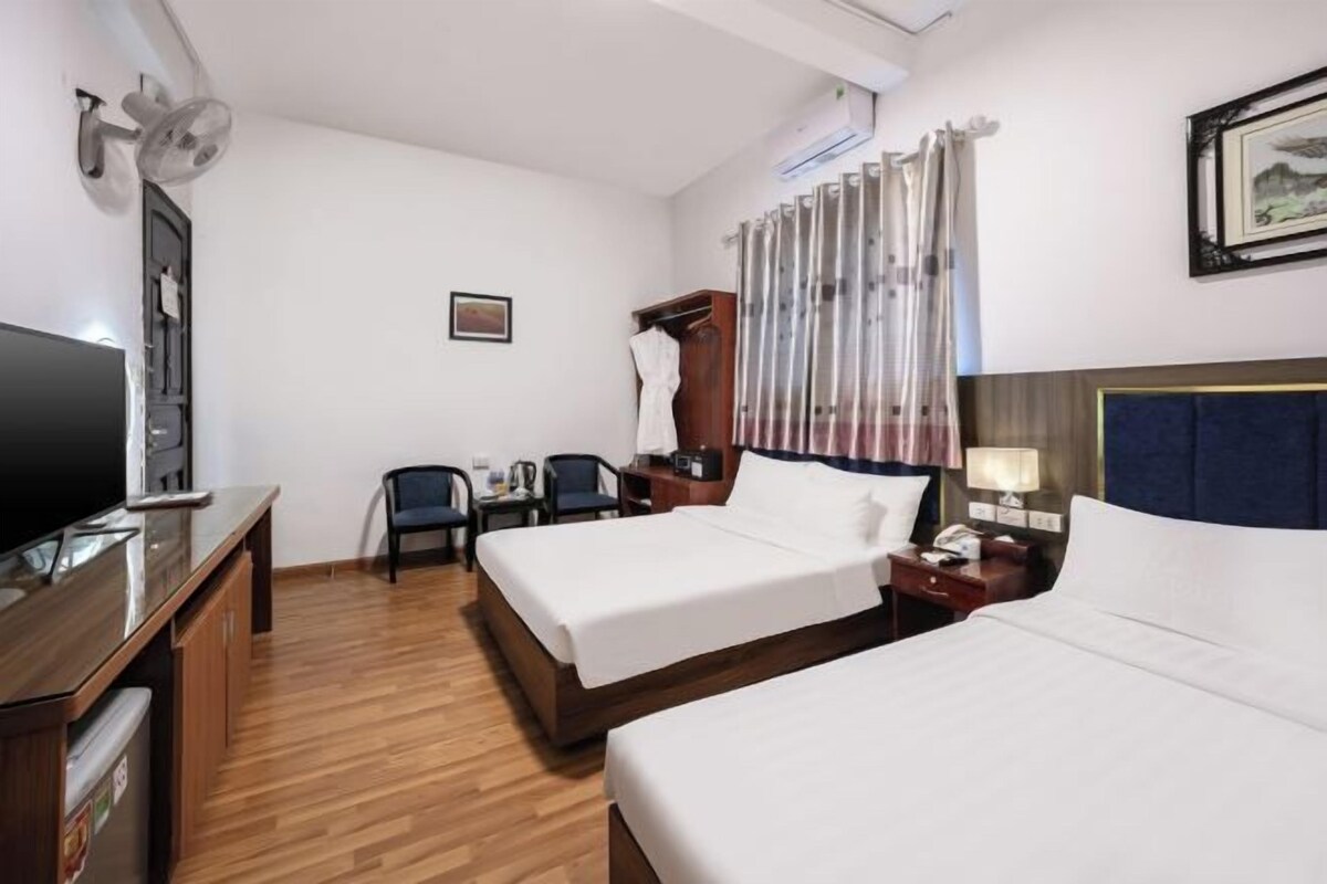 A hotel room with two beds, a desk, a TV, a wardrobe, and a curtain.