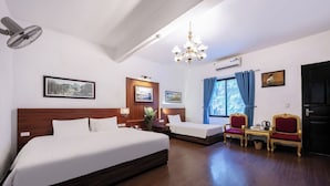 Ein Hotelzimmer mit einem großen Bett, zwei kleineren Betten, einem Schreibtisch mit Stühlen, einer Kristallleuchtre und gerahmten Bildern an den Wänden.