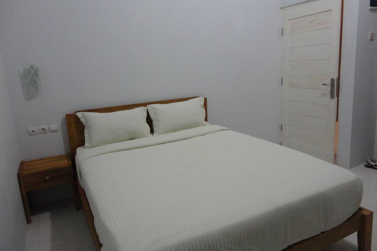 Ein Schlafzimmer mit einem Einzelbett, einem Holzkopfende, einem Nachttisch und einer weißen Tür.