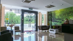 A modern lobby with a glass door entrance, a reception desk, seating area, and a mural of a forest. - LS Hotel (Masai)