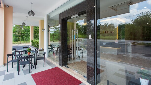 A hotel entrance with a glass door, indoor seating area with tables and chairs, and a red carpet leading to the entrance. - LS Hotel (Masai)