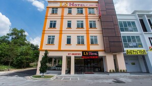 A multi-story hotel with a prominent orange and beige facade, multiple windows, and a visible entrance. - LS Hotel (Masai)
