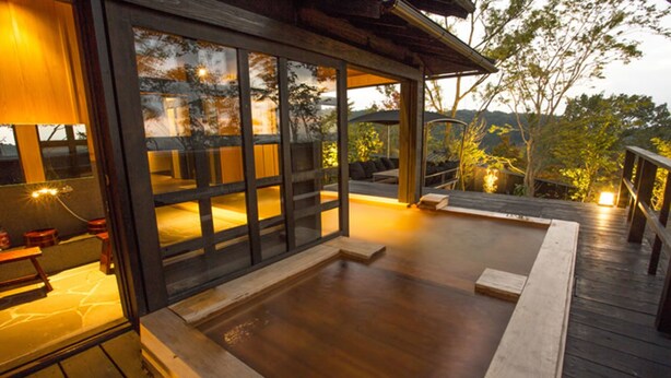 Una terraza de madera con un jacuzzi, un espacio de estar y vistas del paisaje circundante.