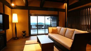 A cozy living room with a sofa, a coffee table, and a lamp. There is a large window with a view of the outdoors.