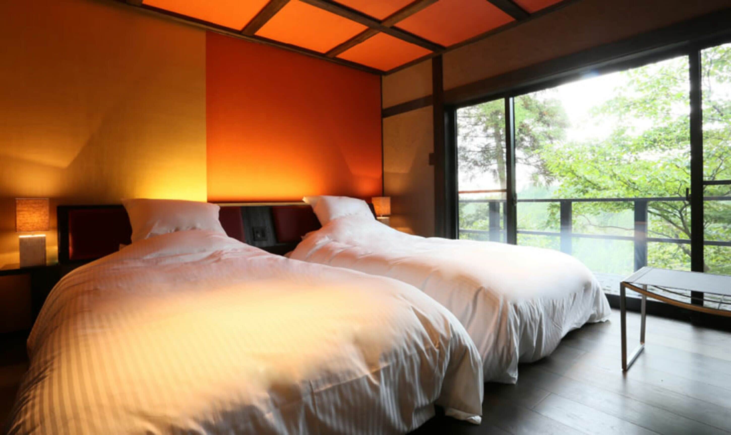 Ein modernes Schlafzimmer mit zwei Betten, einem großen Fenster mit Blick auf Bäume und einem Holzboden.