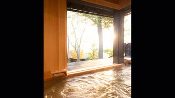Un onsen japonés tradicional con suelo de madera y vistas a árboles.