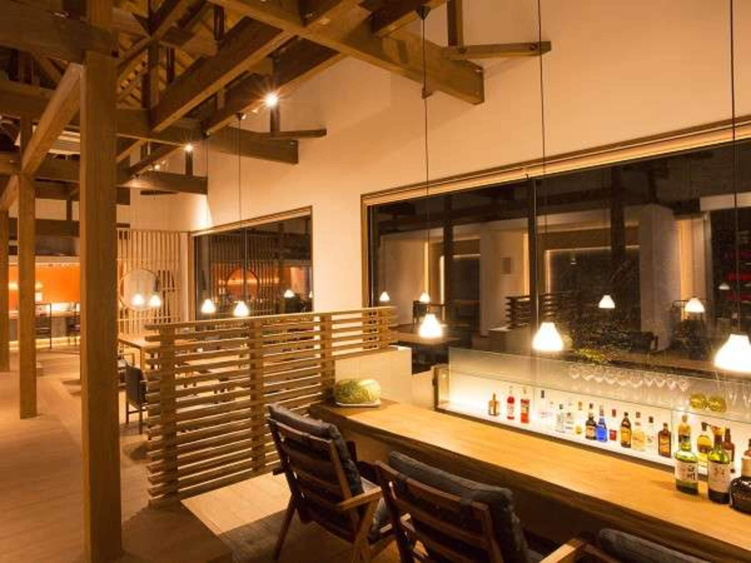 A bar area with a long counter, multiple hanging light fixtures, and a large window.