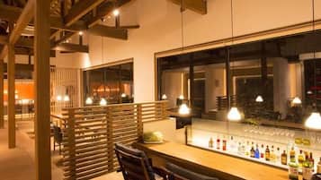 A bar area with a long counter, multiple hanging light fixtures, and a large window.