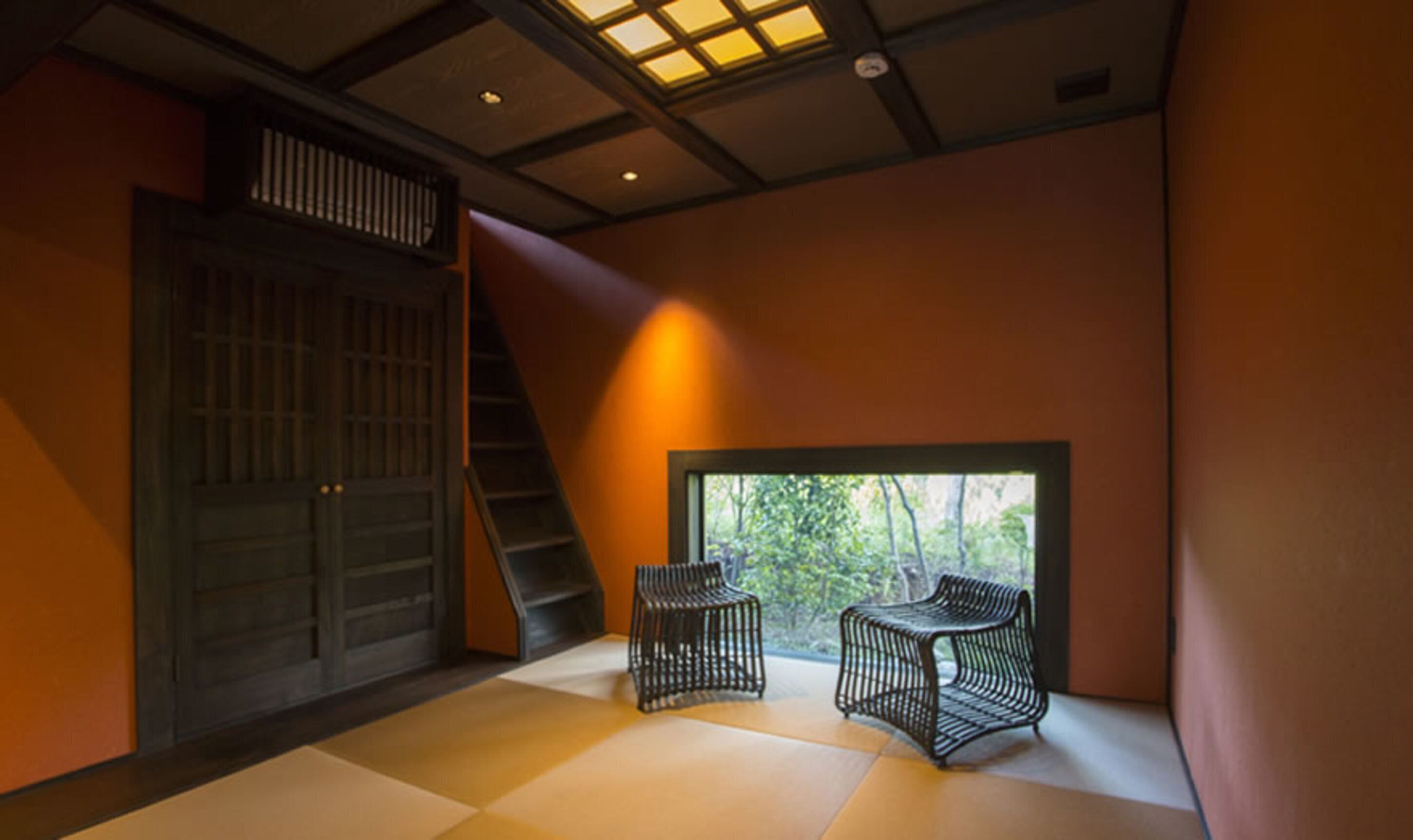 A modern interior with a large sliding door, a staircase, and two black chairs near a window with a view of trees.