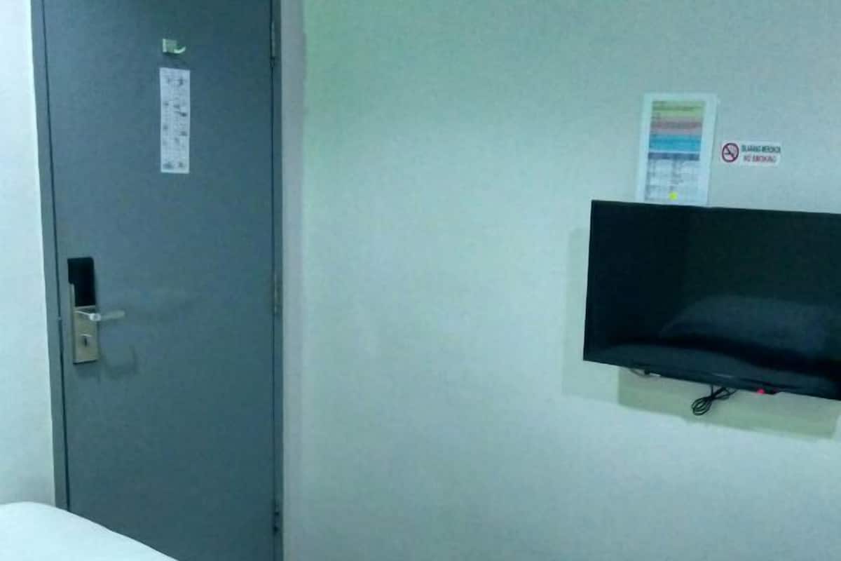 A hotel room with two single beds, a grey door, a flat-screen TV mounted on the wall, and a sign indicating no smoking.