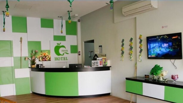 A hotel reception area with a green and white color scheme, a reception desk, a television, and a wooden chair. - Green Hotel (Sungai Besar)